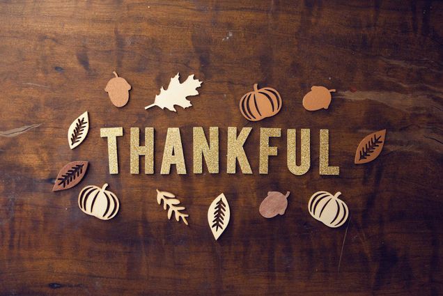 Photo: Small wooden block letters spell out the word "Thankful" on a dark wooden tabletop. Around the word is wooden cutout shapes of varying shades of wood featuring Autumn images like pumpkins, leaves, and acorns.
