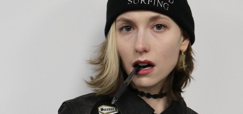 Photo: A woman with short blonde hair wearing a black beanie that says "No Crowd Surfing" and a jacket covered in pins