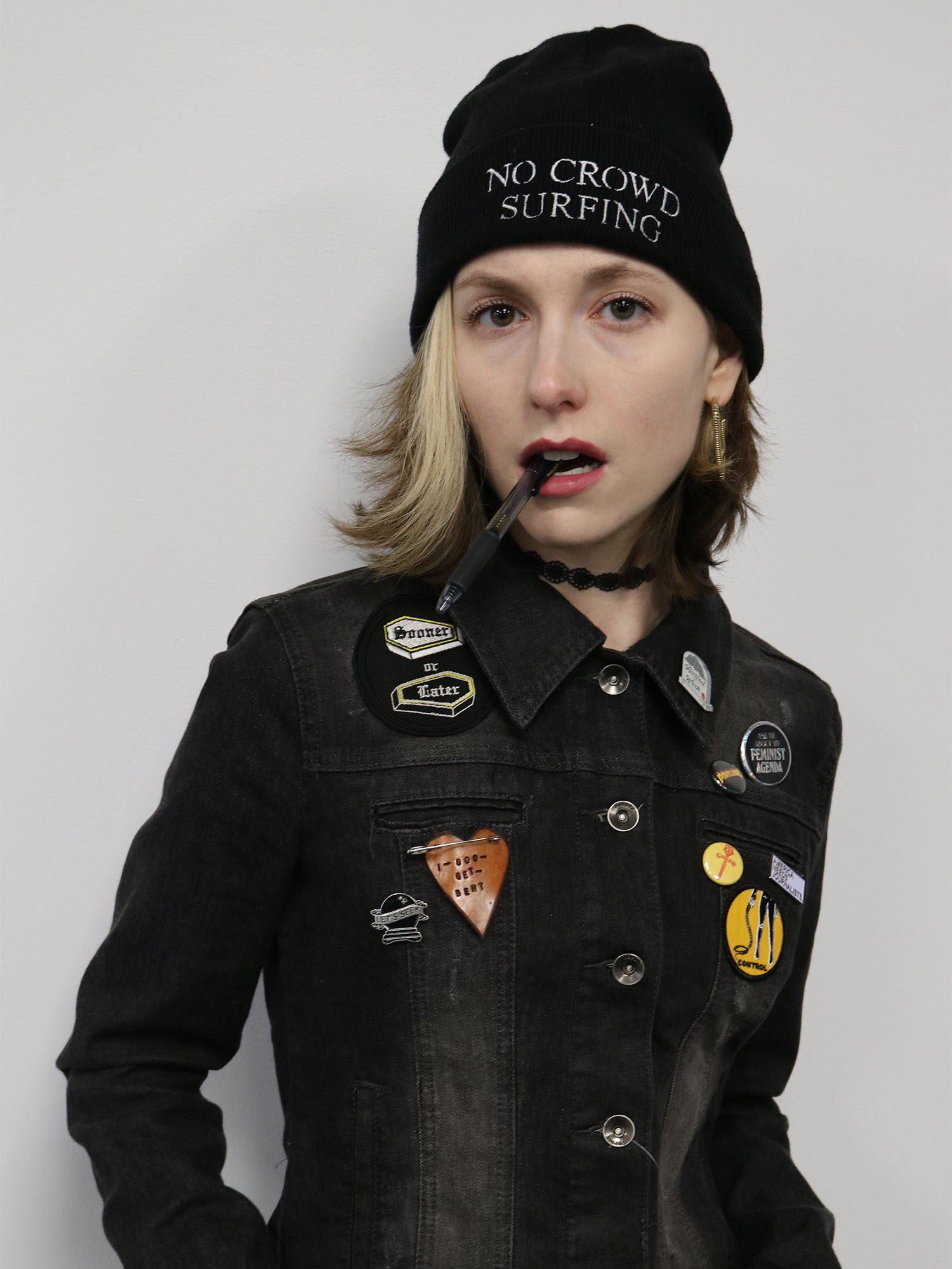 Photo: A woman with short blonde hair wearing a black beanie that says "No Crowd Surfing" and a jacket covered in pins