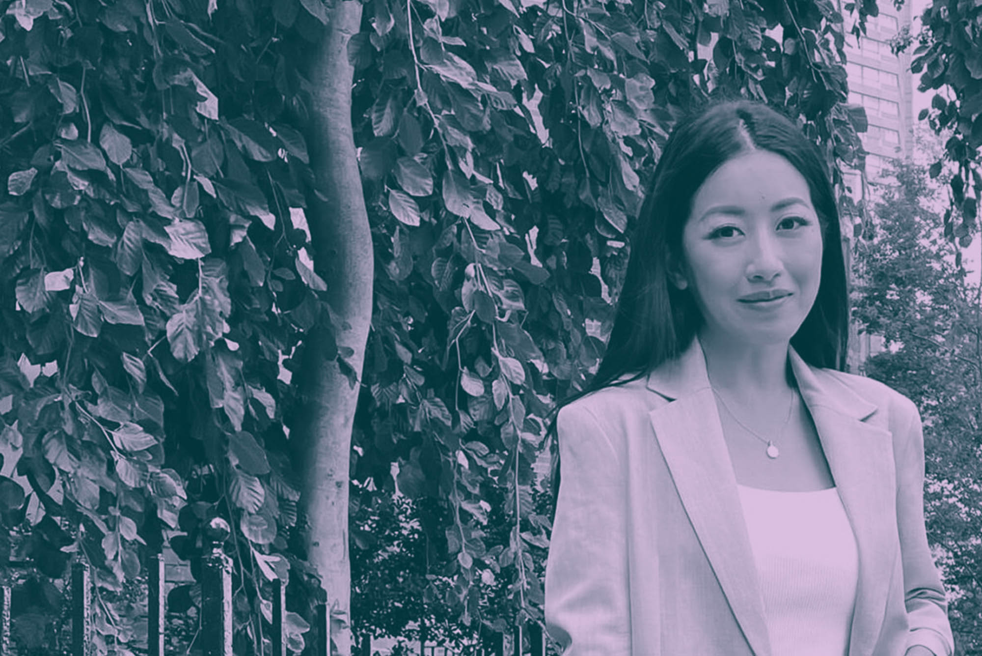 Photo: A young Asian woman with long, straight black hair smiles and poses on a quiet, red brick sidewalk. She wears a whit blouse, beige blazer, and jeans and holds a tan tote bag in her hand. A light purple overlay stylizes the photo.