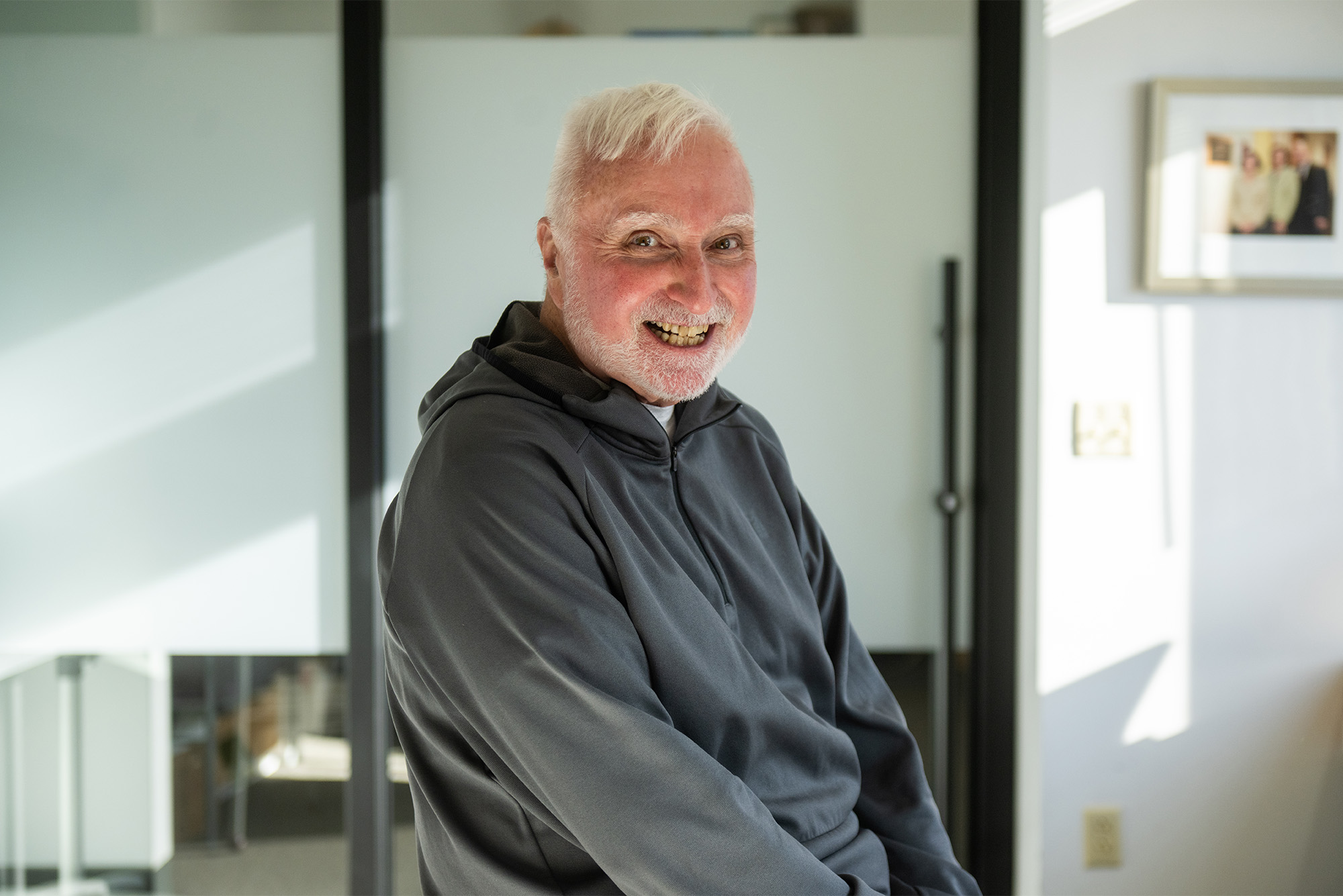Photo: An older man wearing a hooded sweatshirt smiles for the camera in a gym setting