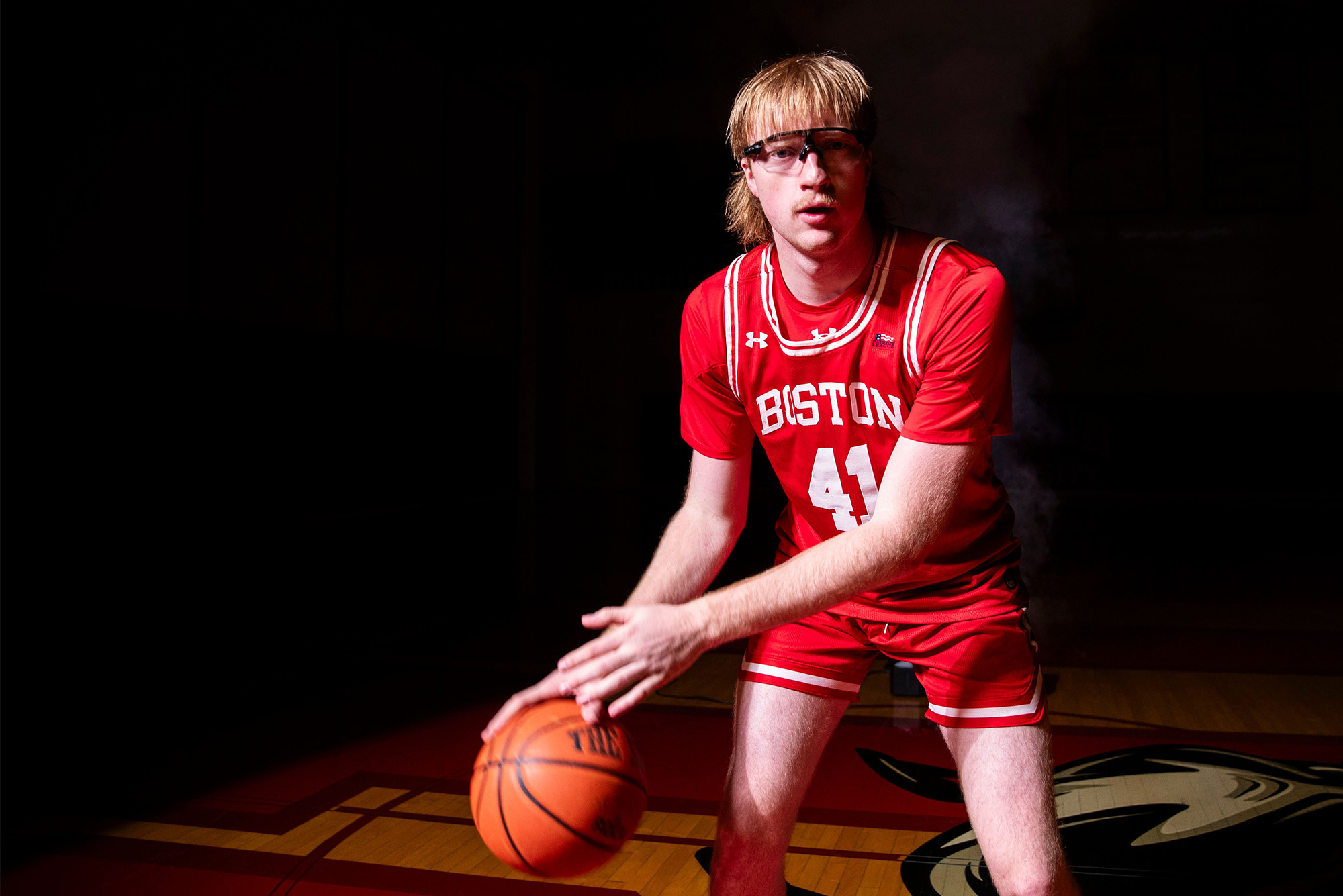 Photo: A college basketball player wearing all red with red hair and goggles dribbling a basketball