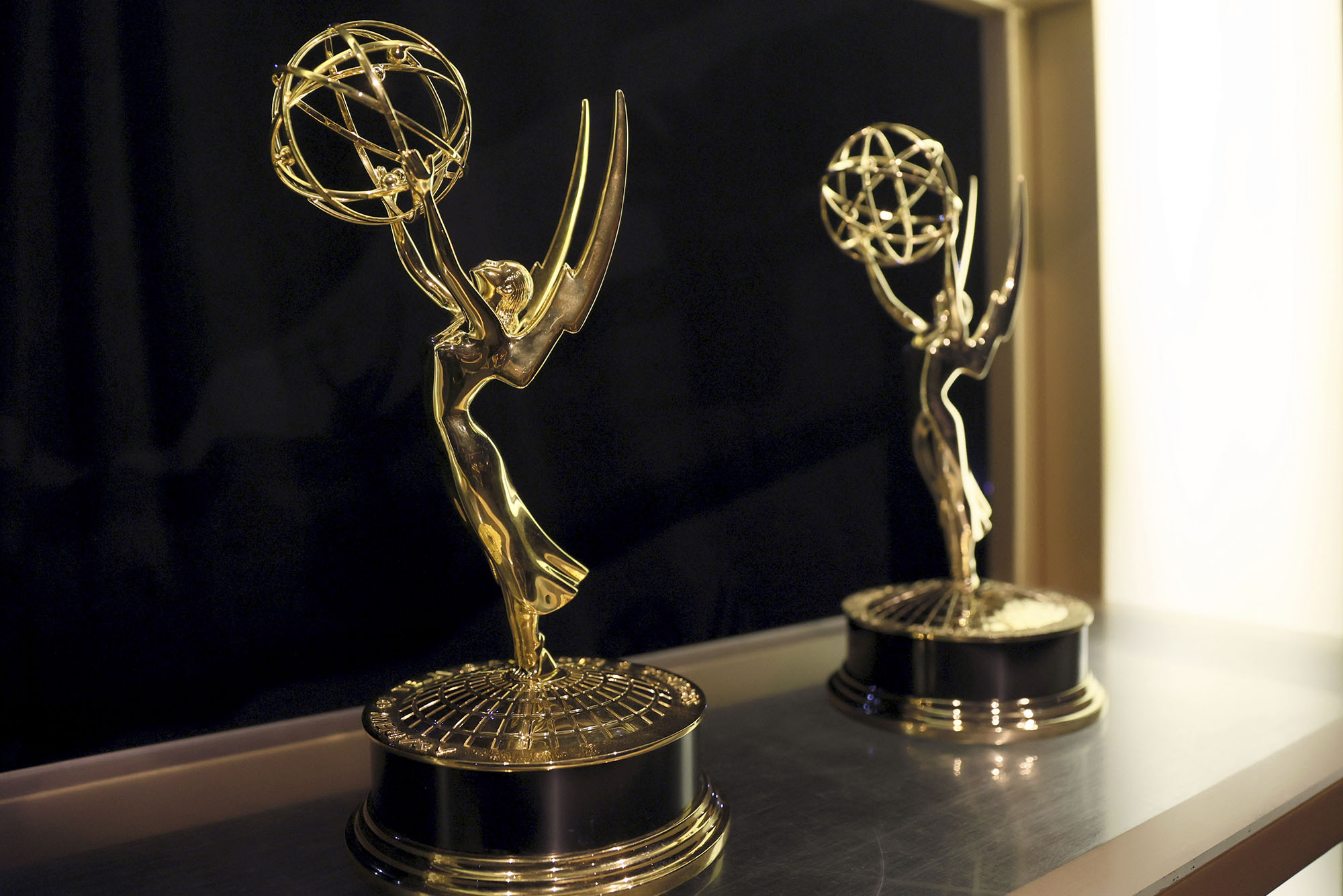 Photo: A stock image of two emmy awards--a golden statue with a person holding a skeleton sphere in a beautiful arch.