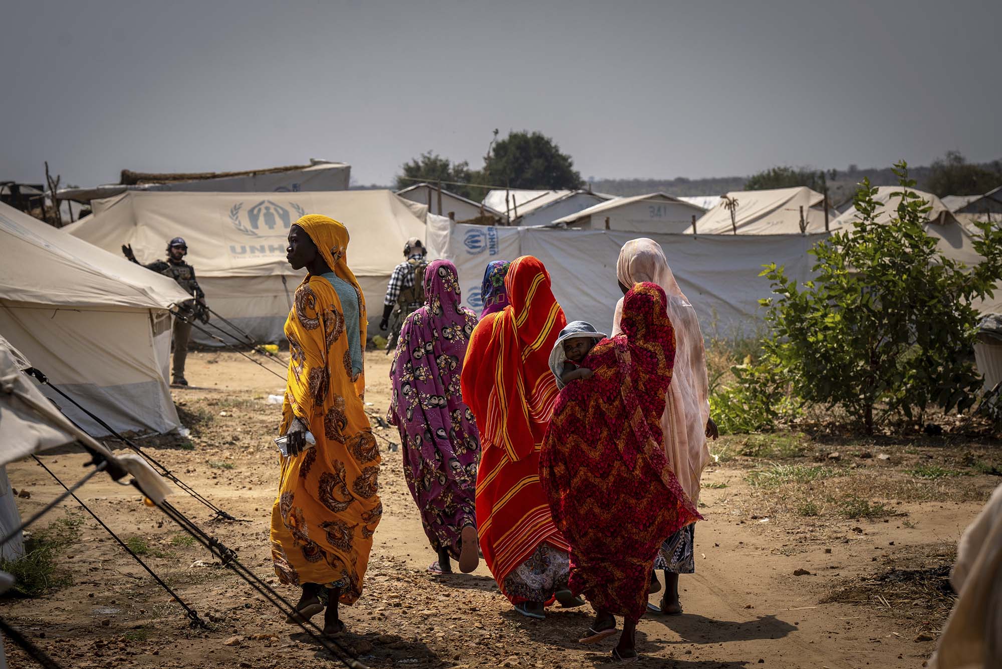 Photo: A group of woman walk in a refugee camp, one with her child wrapped in bright, beautiful garments.