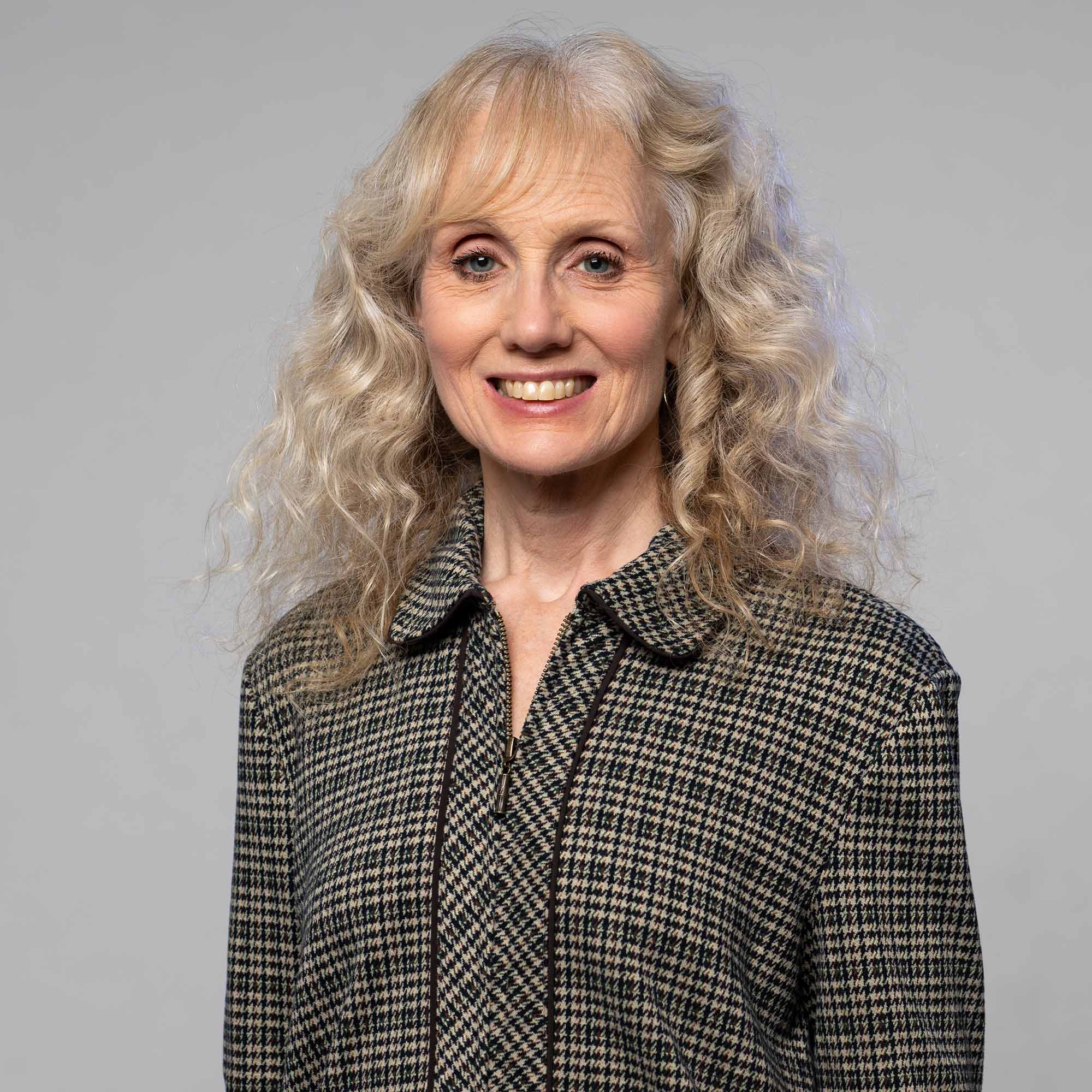 Photo: Portrait headshot of a woman wearing a flannel with long curly hair