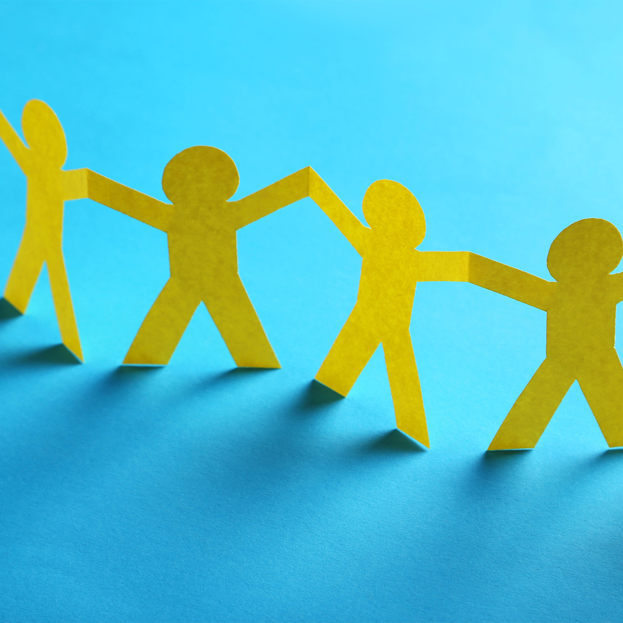 Photo: Paper people hold hands together in front of a blue background