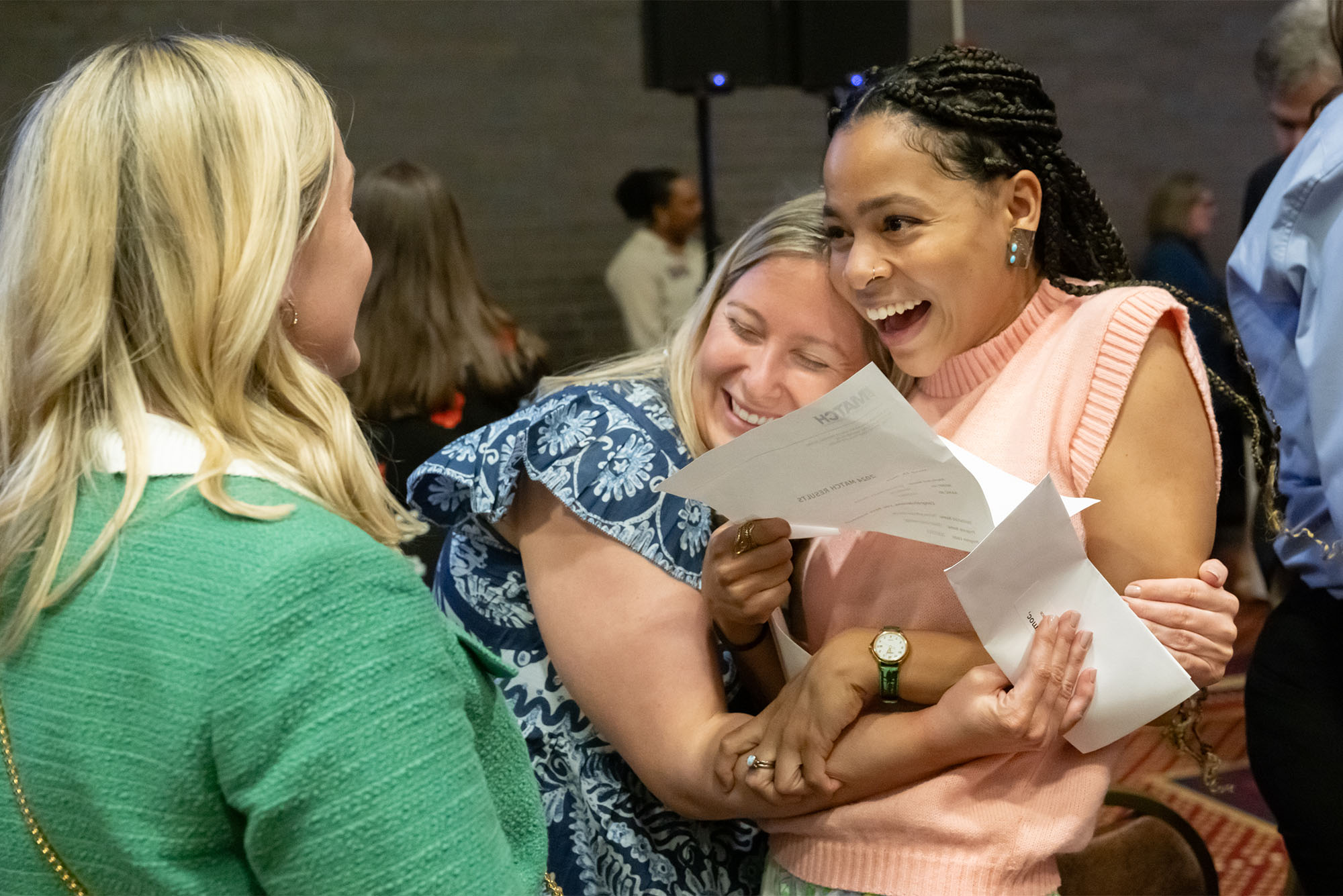 Photo: A woman with braids holding a sheet of paper is embraced in a hug by a woman wearing a blue patterned dress at a Medical Student Match Day celebration at Boston University