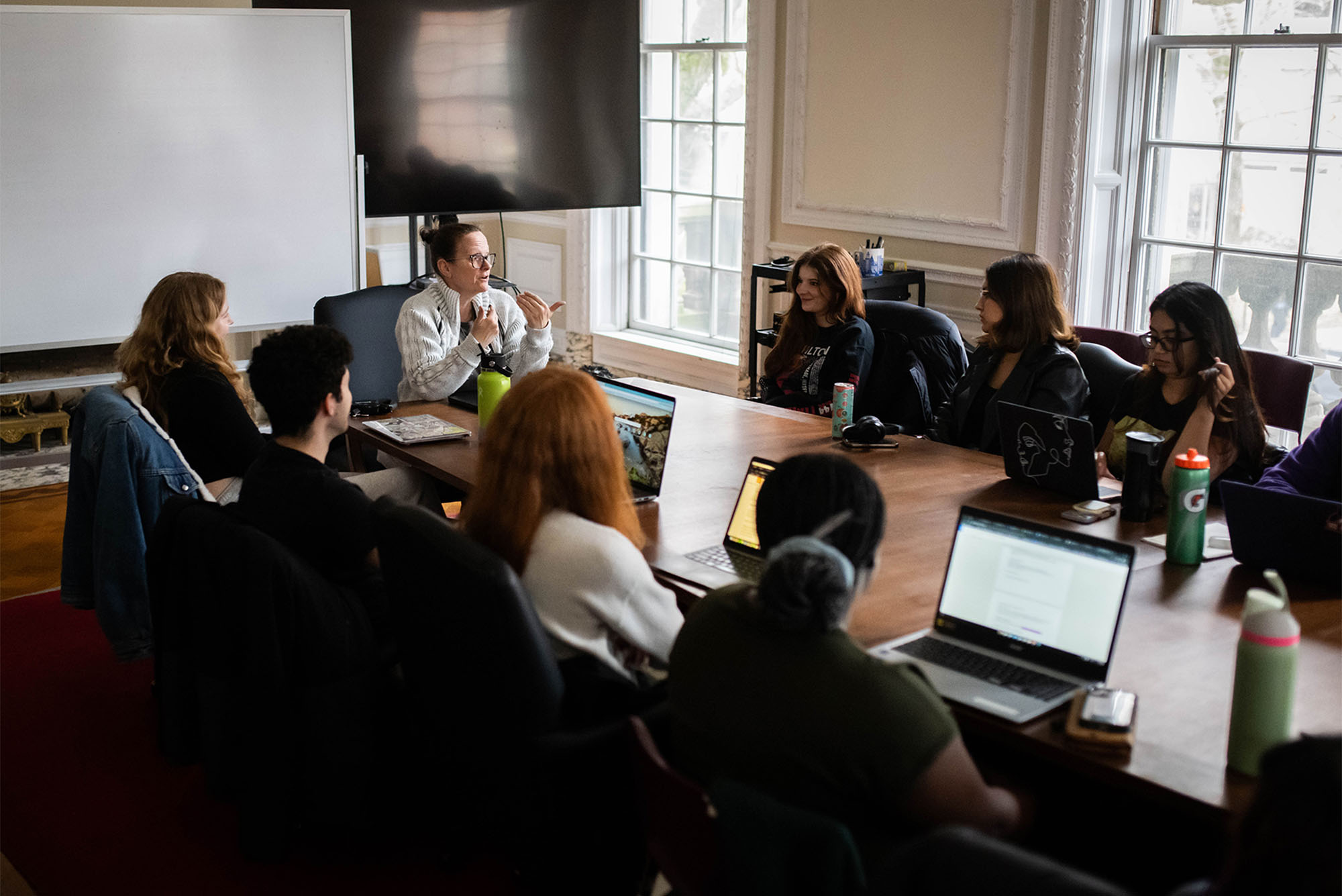 Photo: A classroom of people sitting around a large table with laptops open