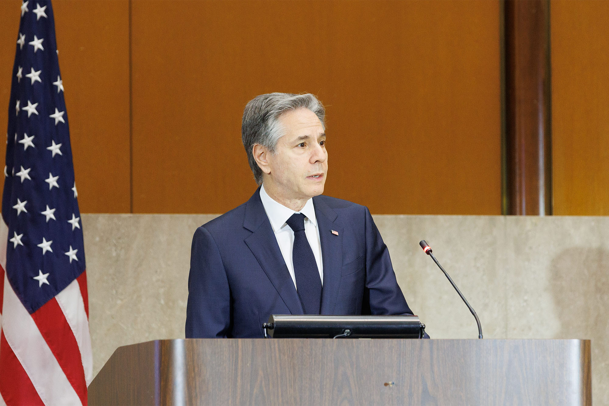Photo: Secretary of State Antony Blinken wearing a suit standing at a podium