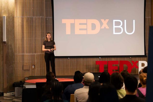 Photo: Marie Grochowski (CAS’26) gave a talk titled “What Fungi Can Teach Us About Global Immigration” at the annual TEDxBU conference. A woman stands in front of a large audience and the words "Tedx BU" are on the screen behind