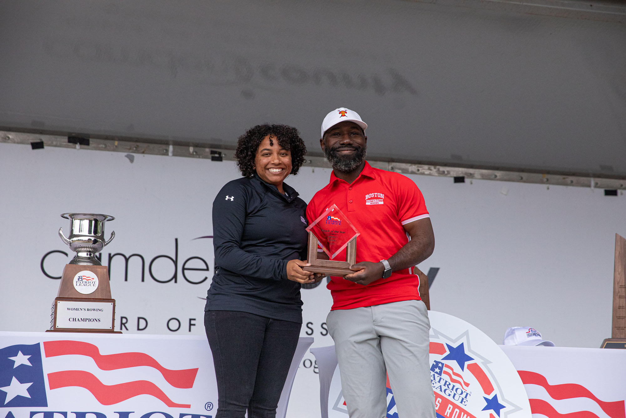 Photo: A picture of two people smiling and holding an award. On the left is a woman wearing a black long-sleeve shirt and on the right is a man in a red, short-sleeve polo that says "Boston University Rowing"