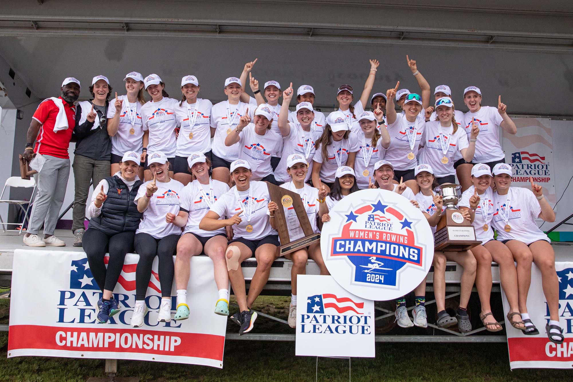 Photo: A picture of the BU Women's Rowing team smiling and posing around a sign that says "Women's Rowing Champions 2024"