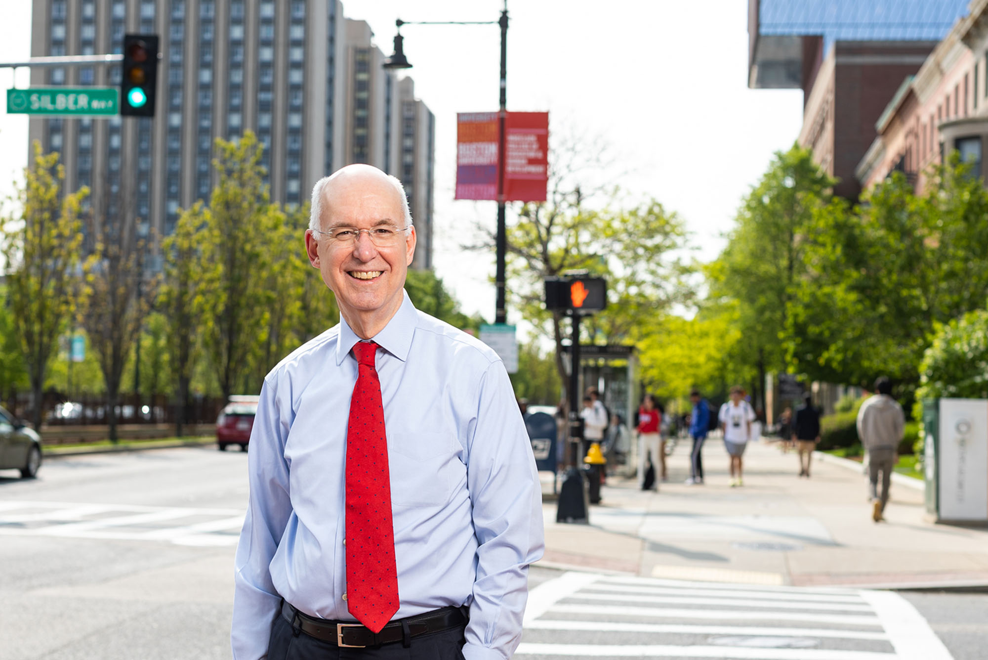 Photo: Interim BU president, Kenneth Freeman, stands in a collared shirt and red tie on a sunny day on Commonealth Ave, an urban scene of Boston University in the background
