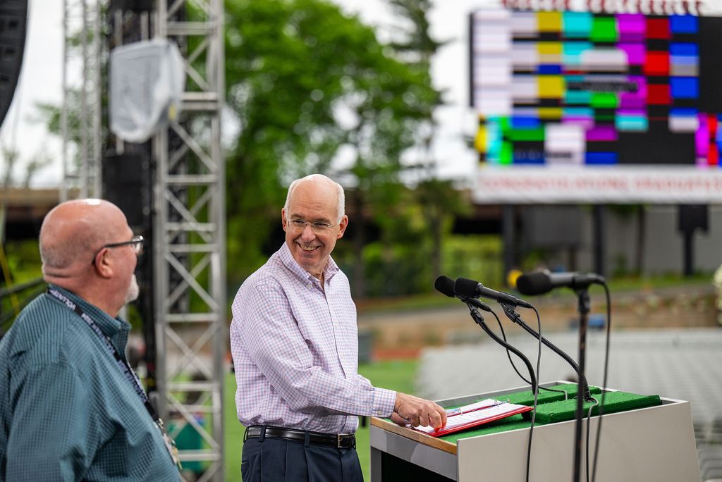 Photo: A picture of two men on an outdoor stage behind a podium with microphones