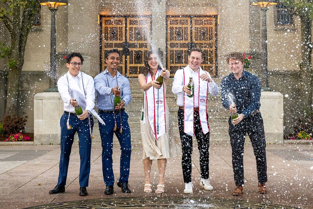 Photo: A picture of five students celebrating and spraying champagne bottles while dressed in semi-formal attire