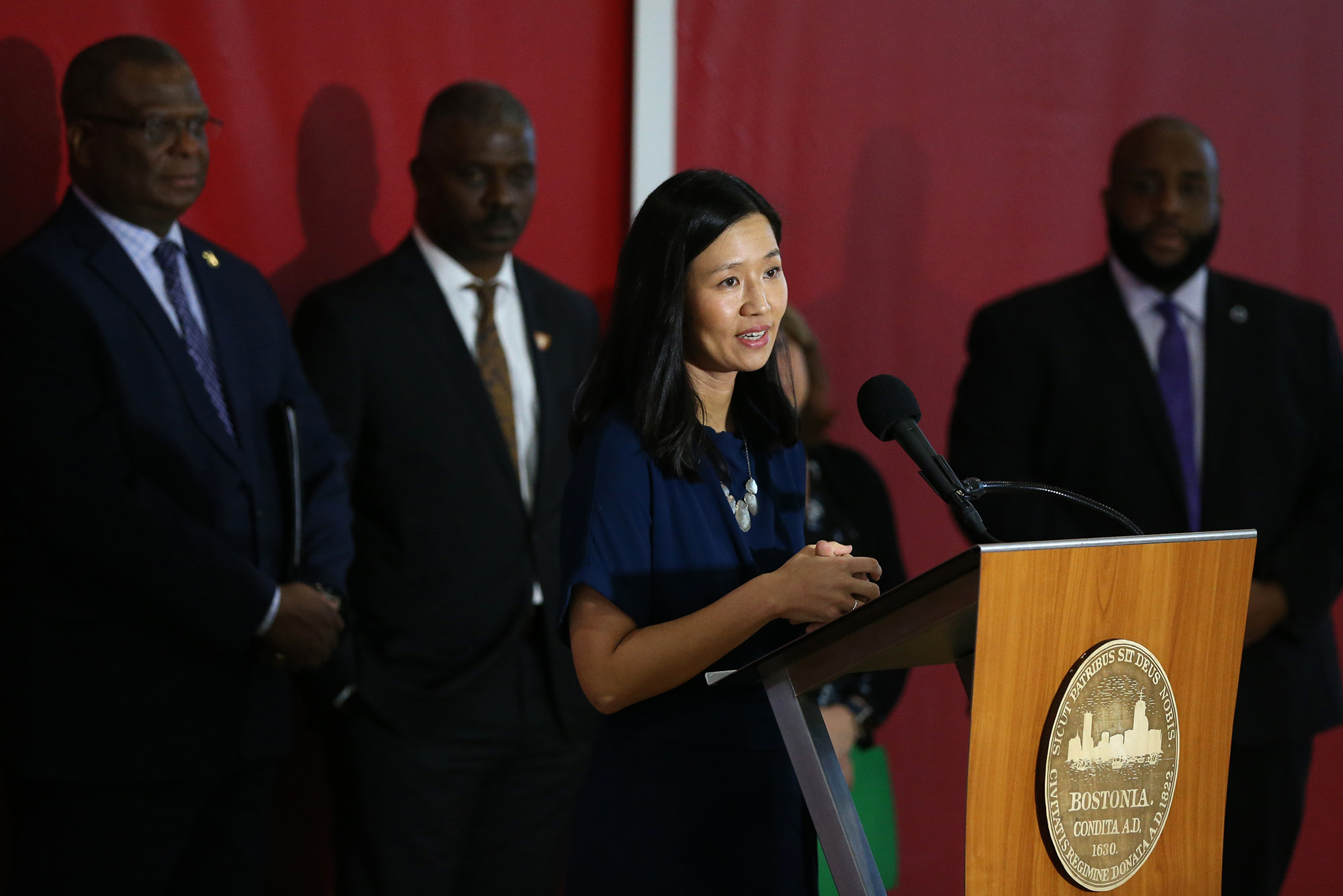 Photo: A picture of Boston Mayor Michelle Wu behind a podium speaking. She is wearing a blue, short-sleeve dress