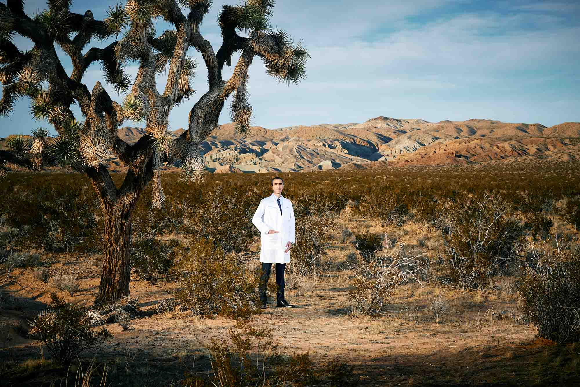 Photo: A doctor stands in the middle of a barren landscape with his hands in his white coat pockets.