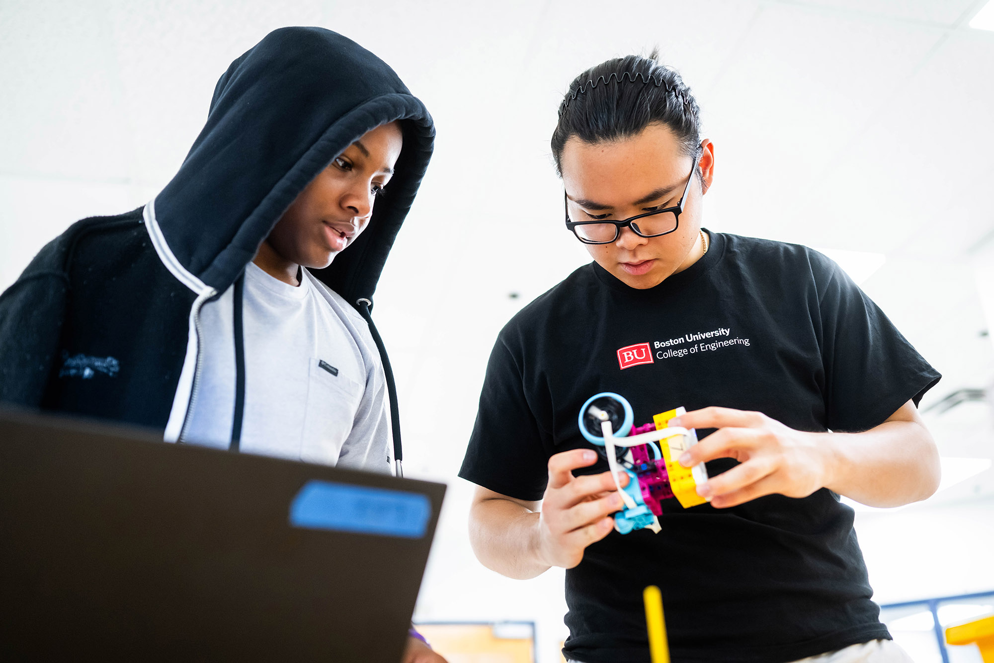 Photo: Jefferey Sheu (ENG 26), on the right in a black tshirt, helps Jahvel Sylvestre, on the left in a black hoodie, with his race car during Design: Intro to Robotics