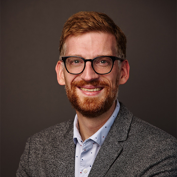 Photo: A white man wearing glasses and a suit with a collared shirt poses for a formal portrait