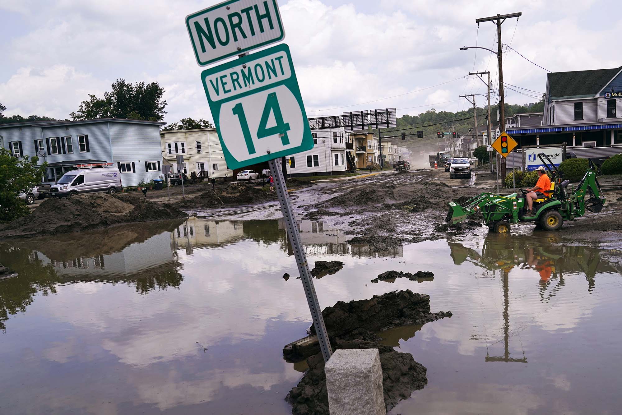 Photo: A small tractor clears water from a business as flood waters block a street.