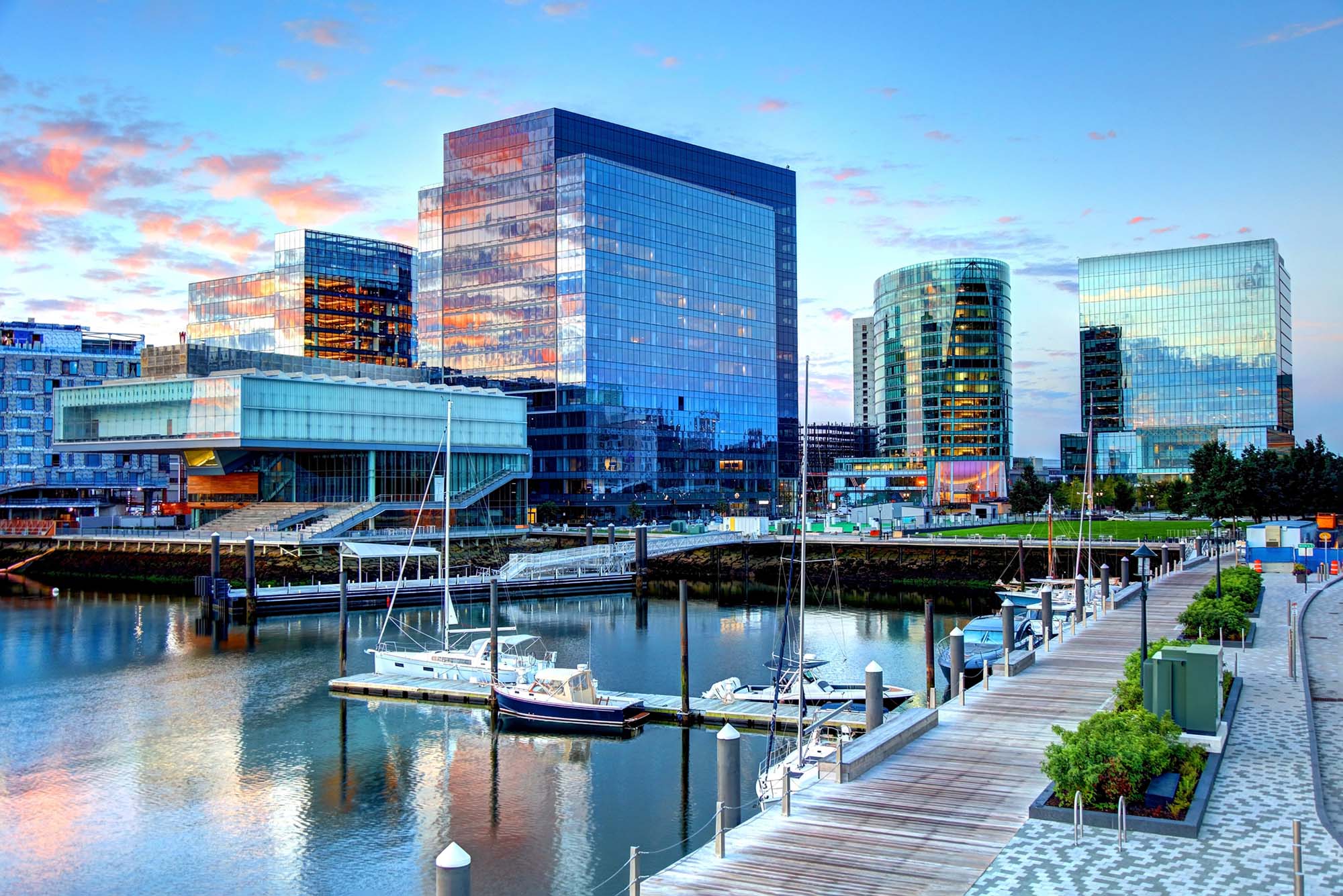 Photo: A picture of Boston's Seaport district. There are modern, glass skyscrapers in front of the Boston harbor