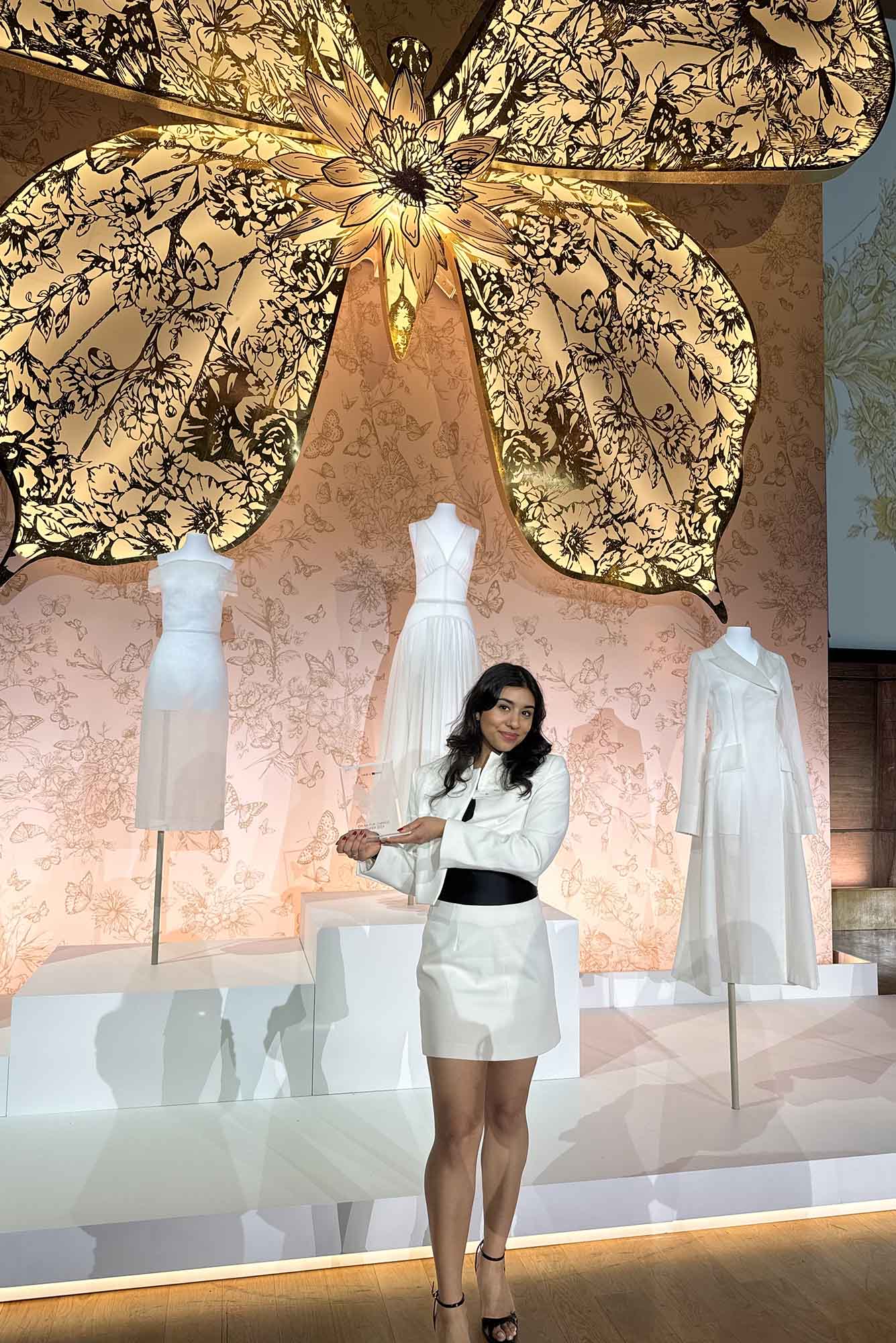 Photo: A young woman in a white skirt suit set poses in front of an installation for Dior.