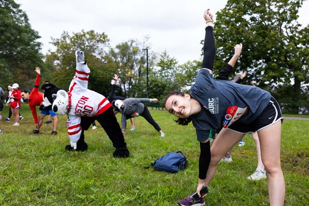 Photo: A runner stretching with BU's mascot, Rhett, before the 2023 5K Fun Run through the Charles River Esplanade during last year’s Alumni Weekend.