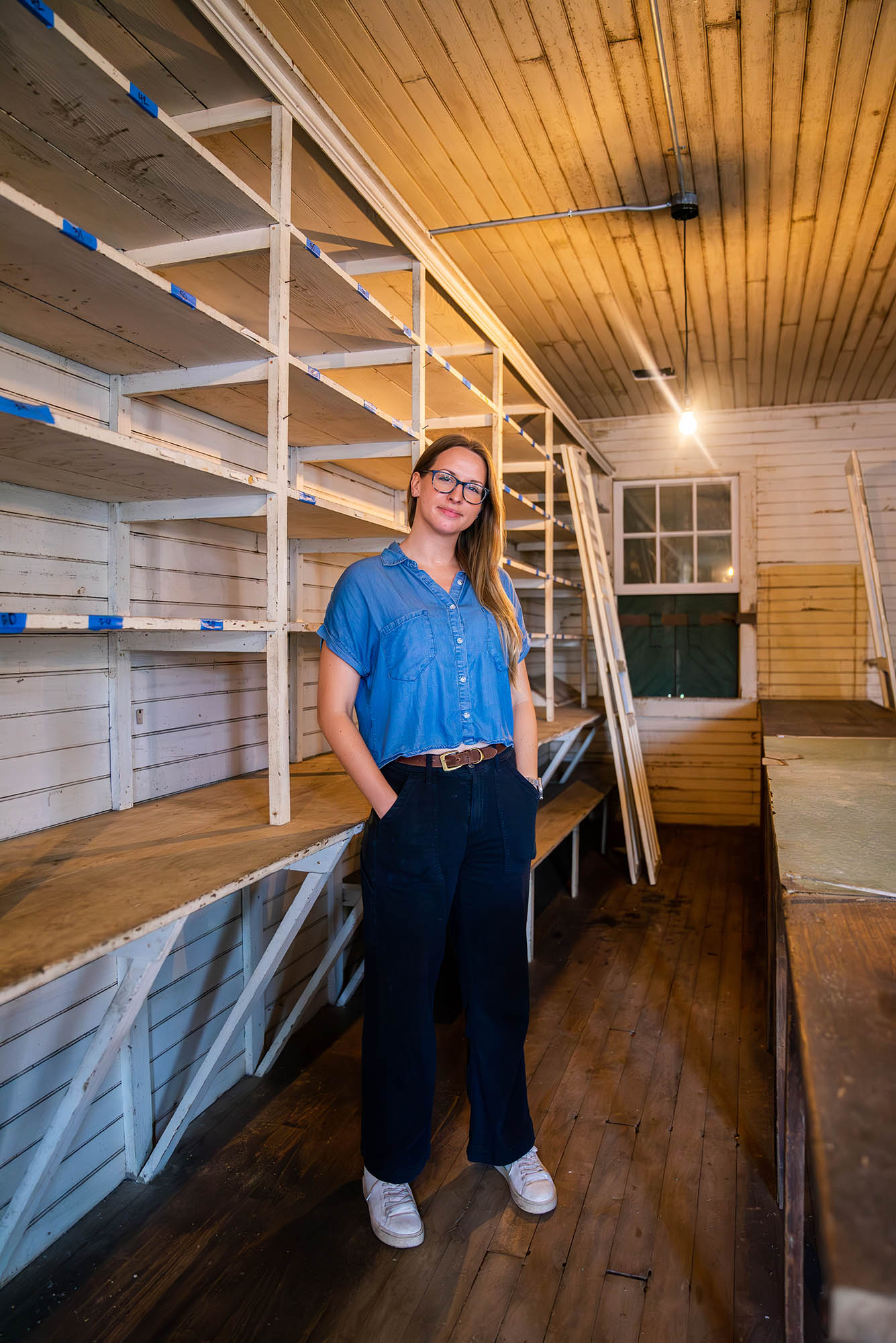 Photo: Mary Snyder, a white woman with shoulder length hair, is a BU PhD student in the American Studies program. She stands in a room with rows of wooden bare shelves. Photo: Mary Snyder, a white woman with shoulder length hair, is a BU PhD student in the American Studies program. She stands in a room with rows of wooden bare shelves.