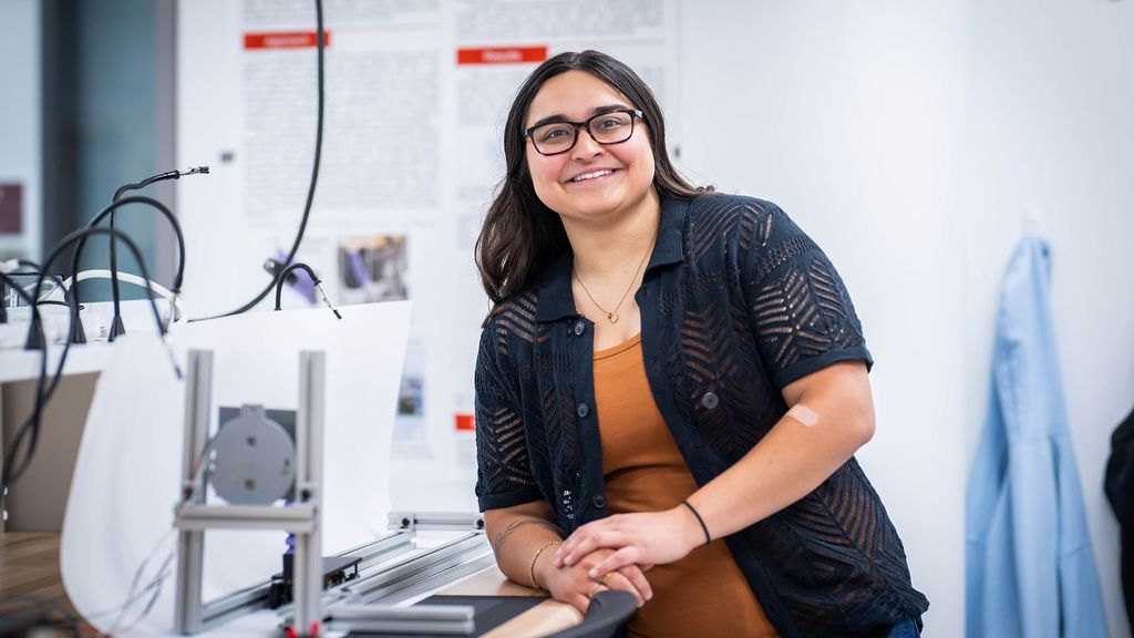 Photo: A woman with dark hair and glasses smiling and posing in a lab