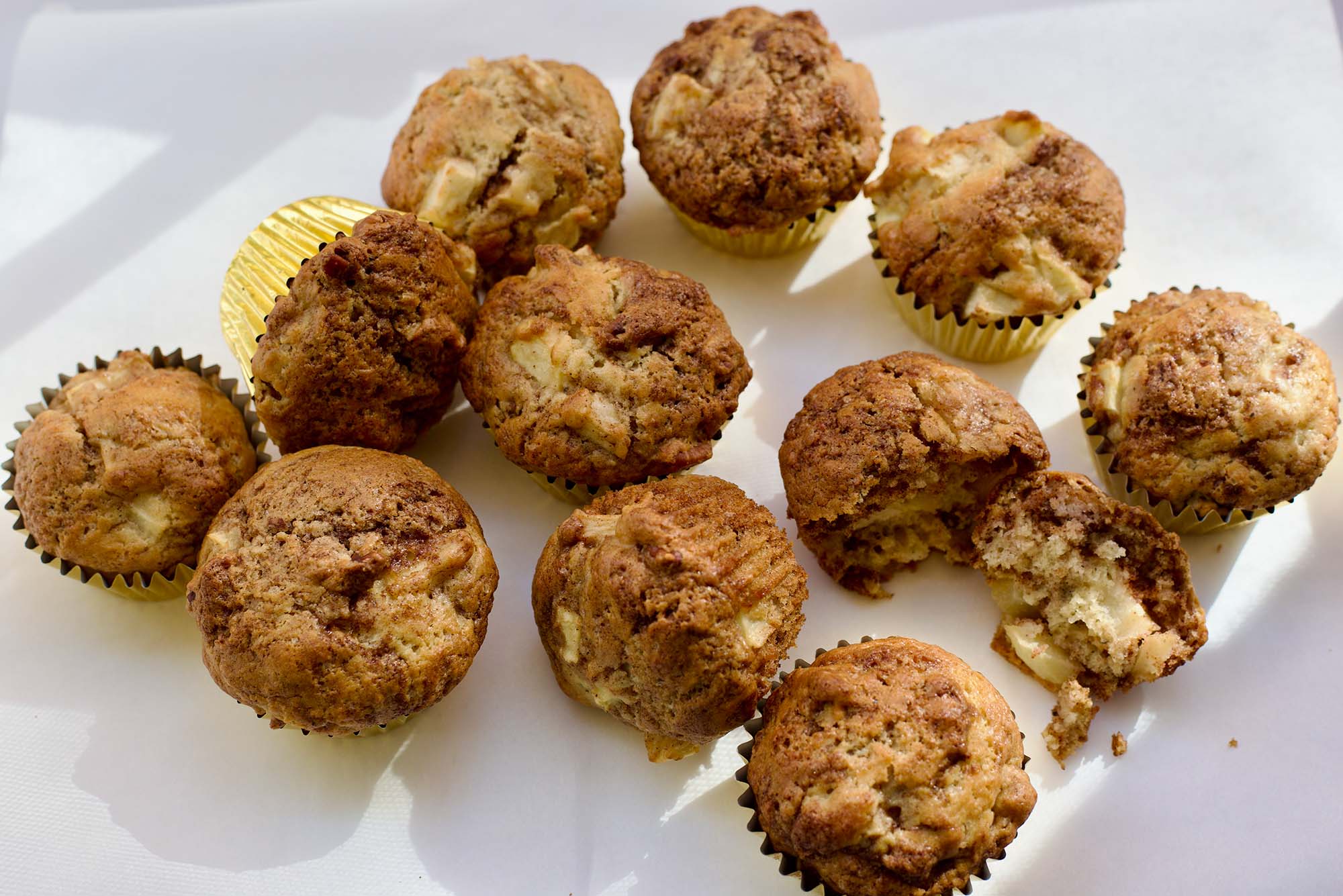 Photo: A picture of muffins in golden tins on a white surface. Some are sitting straight up and others are fallen on their side