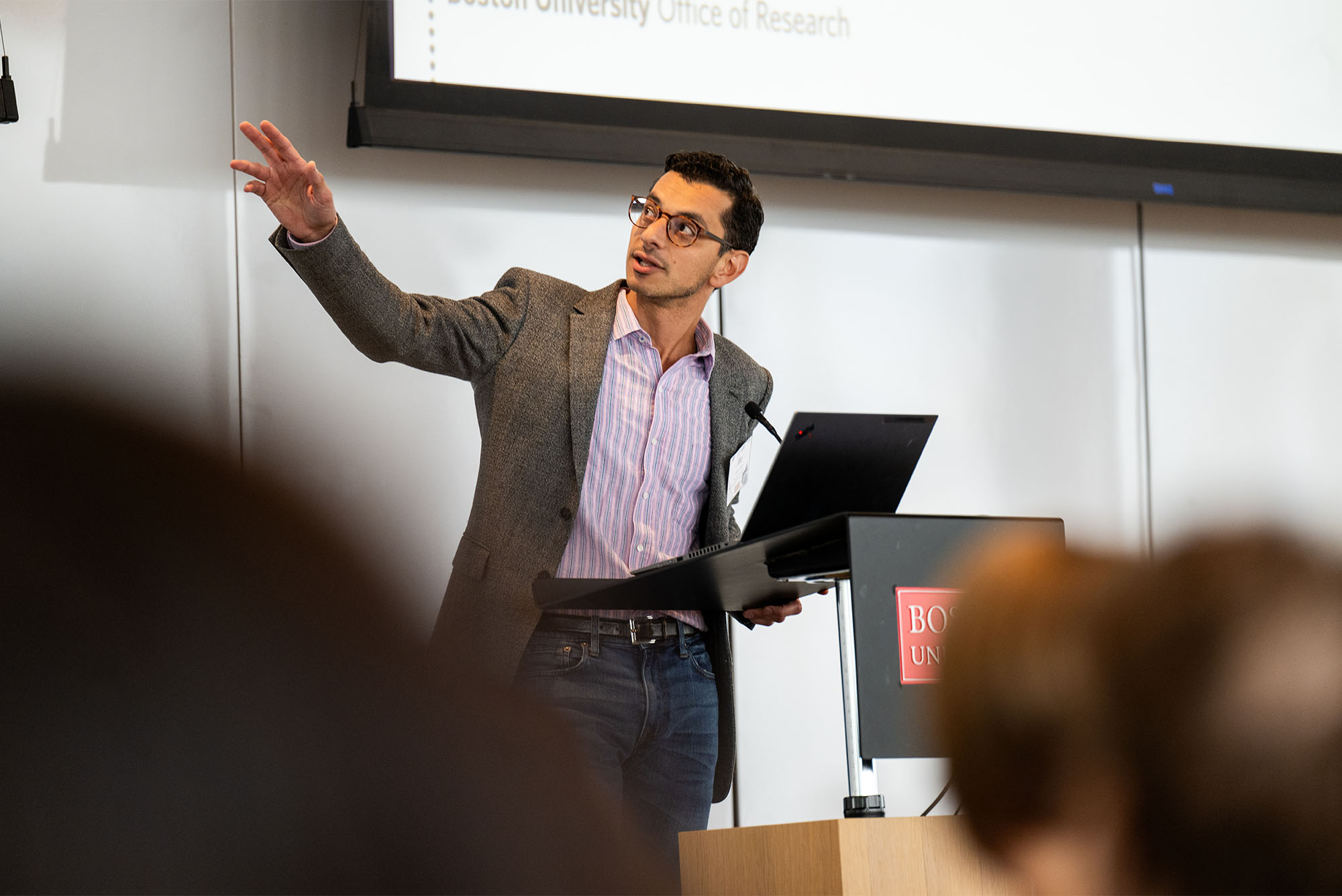 Photo: A presenter gestures toward a screen during a presentation at a research event at BU