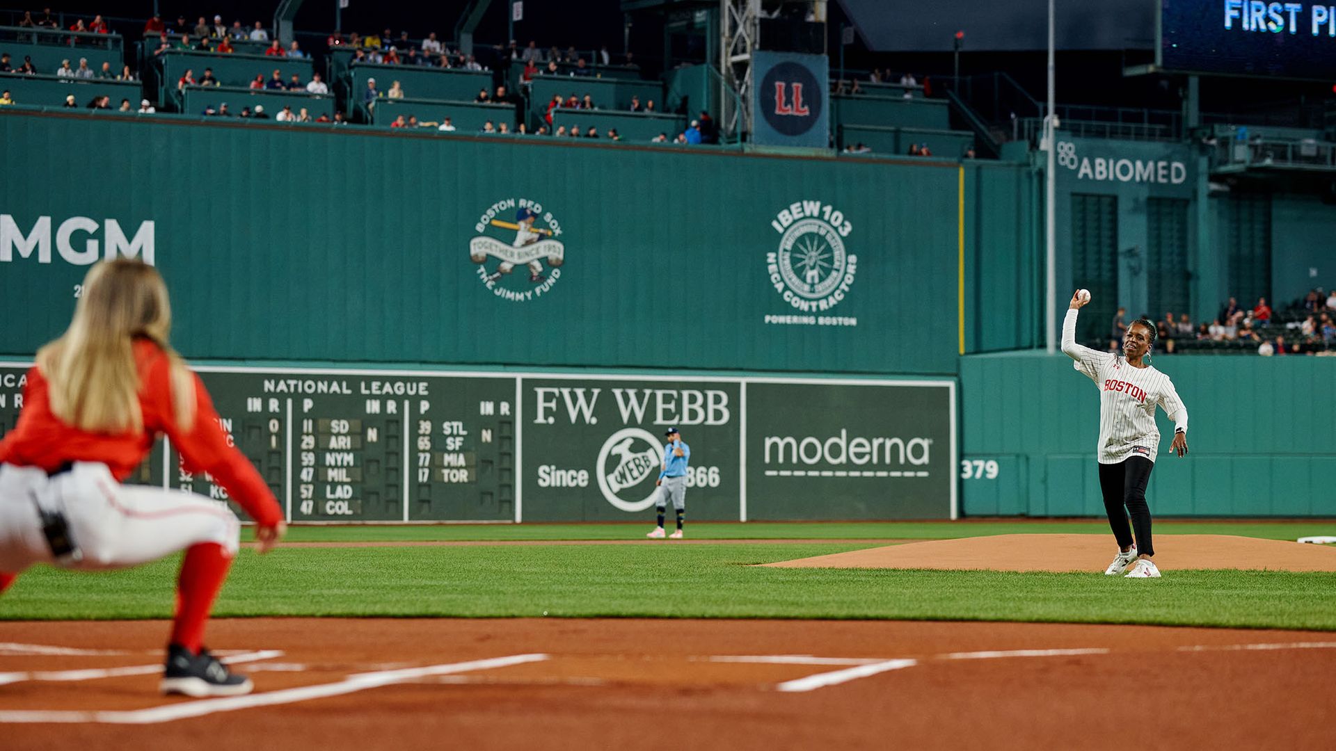 Photo: Melissa Gilliam, a black woman with short dark hair wearing a Red Sox jersey throws the ceremonial first pitch at a recent Red Sox game night honoring Boston University