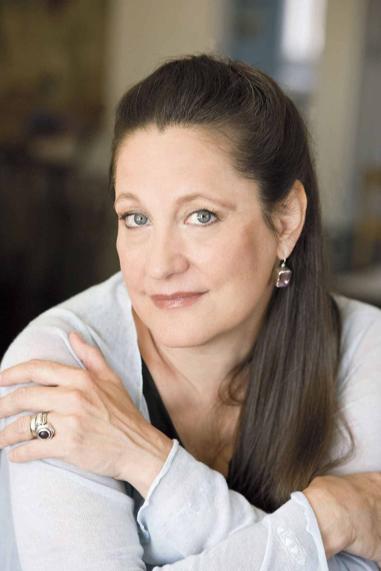 Photo: A white woman with her brown hair pulled back. She wears silver jewelry and a white top.