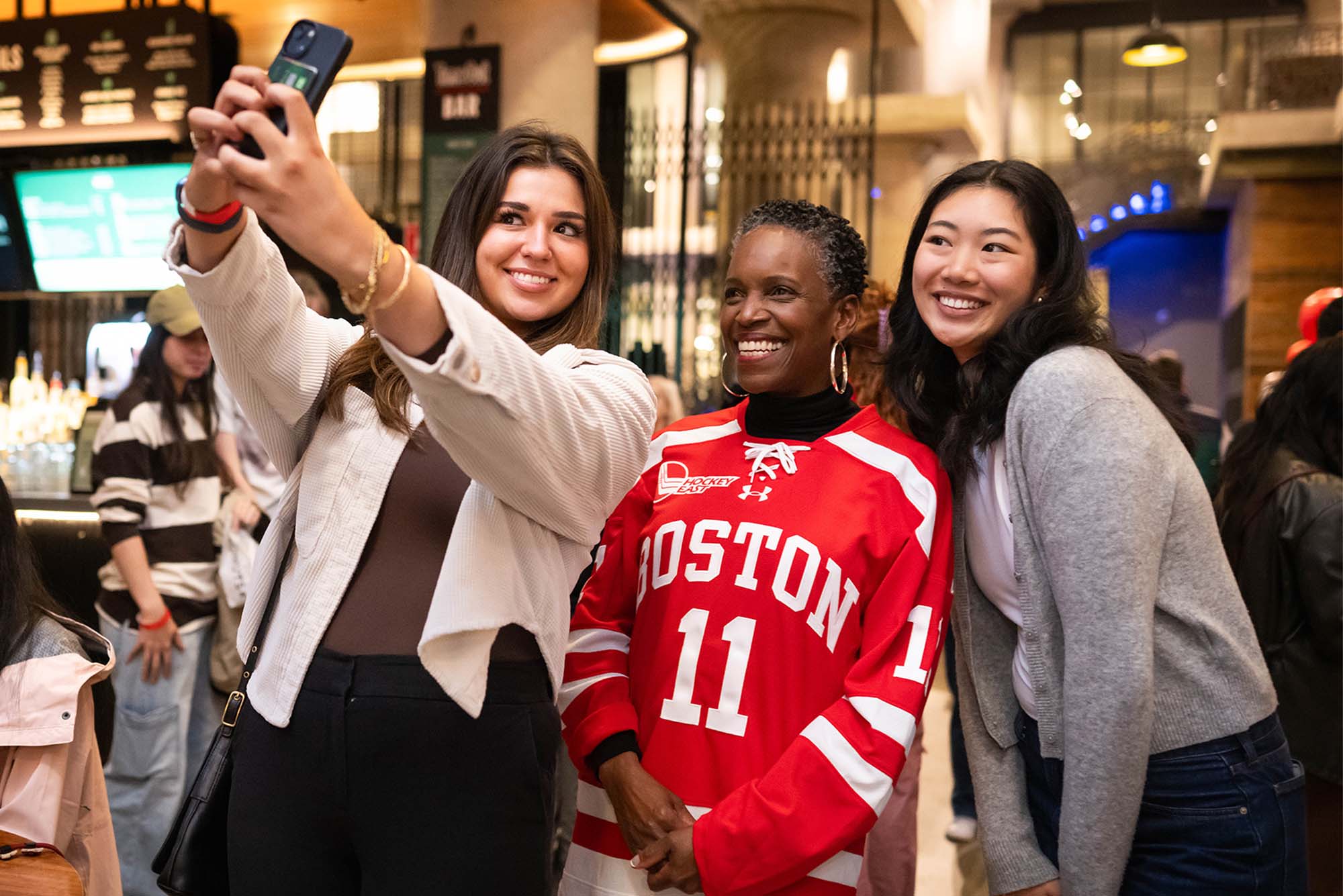 Sophia Caffrey (left) (COM 25) and Kayla Lok (COM 27) take a selfie with President Melissa Gilliam during BU Night at Time Out Market on September 23, 2024. The evening was for students to meet President Gilliam, this indoor “block party” will featured music from a jazz combo of BU students, free swag, and discounted food and drinks for students.Jackie Ricciardi for Boston University Photography