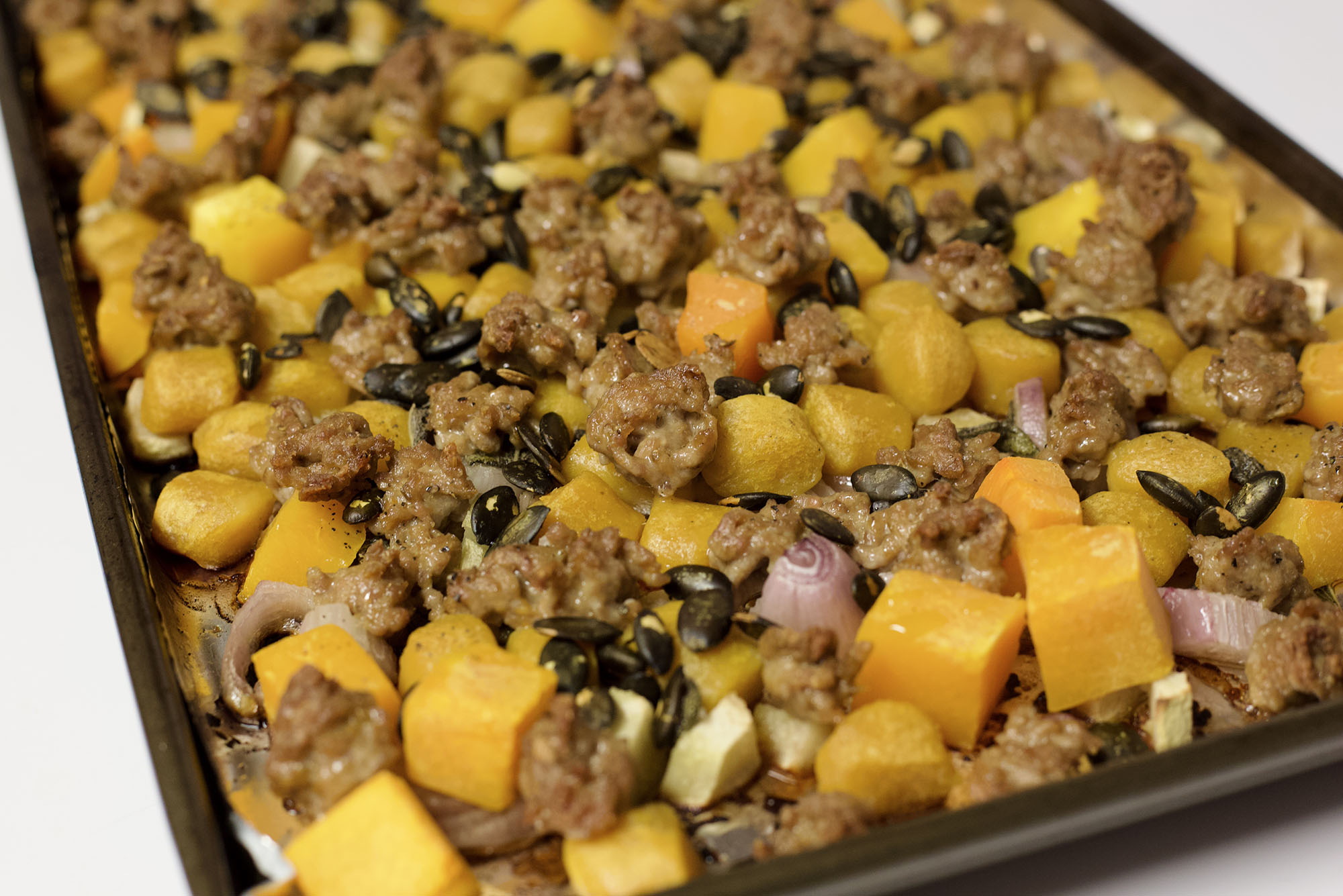 Photo: A close-up of various squash, meat, onions, and shallots on a sheet pan.