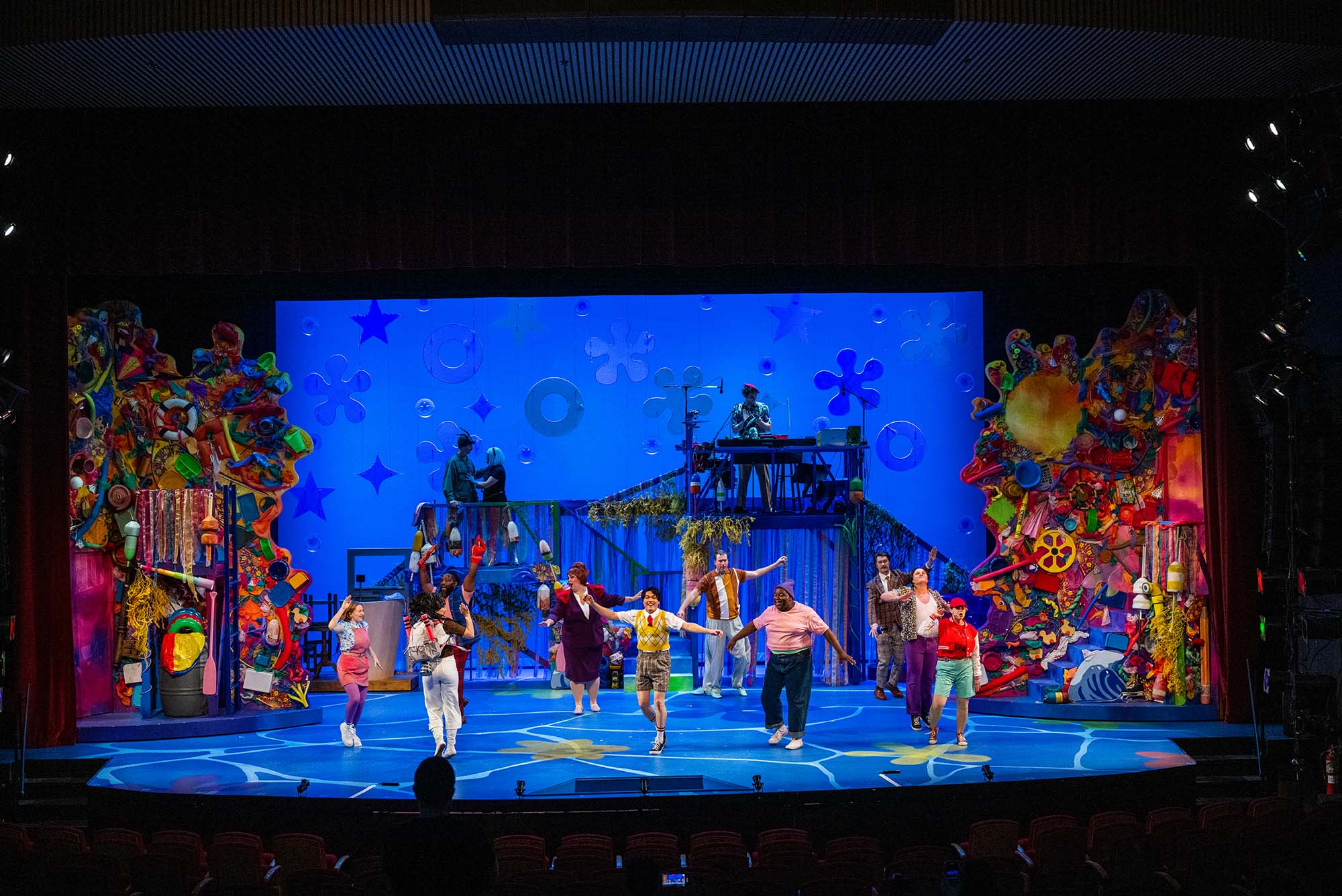 Photo: A wide shot of the stage during the Wheelock Family Theatre's production of "The Spongebob Musical." The set features lots of blues, to simulate being underwater, and the actors are in colorful attire. Along the side of the stage is colorful stacks of memorabilia