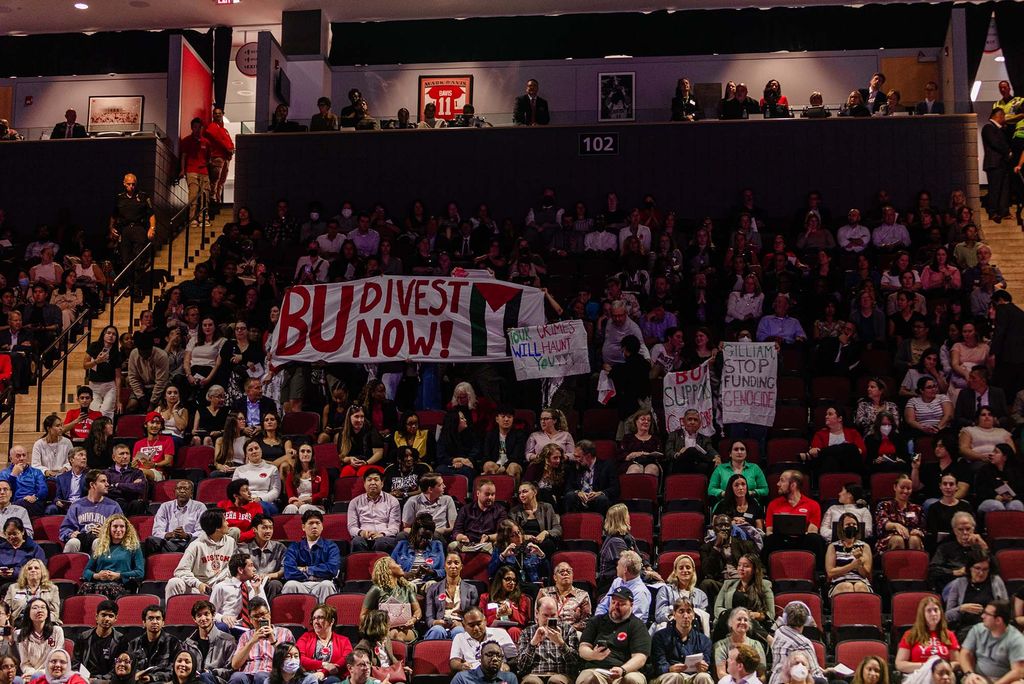 Photo: A small and brief student protest caused a brief disruption of the ceremony. Students hold up banners that read BU DIVEST NOW!