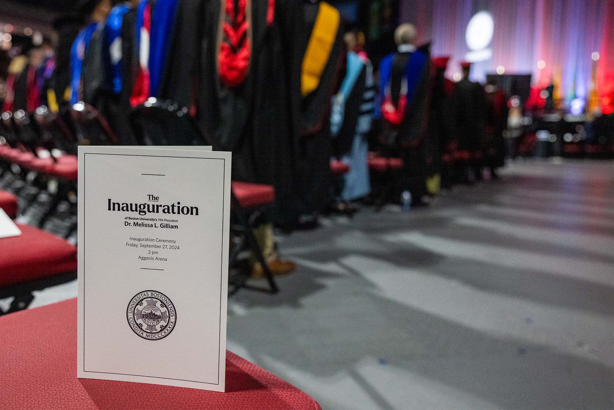 Photo: Program for Melissa L Gilliam's inauguration at BU's 11th President in September 2024, sitting on a chair at the event as the crowd applauds