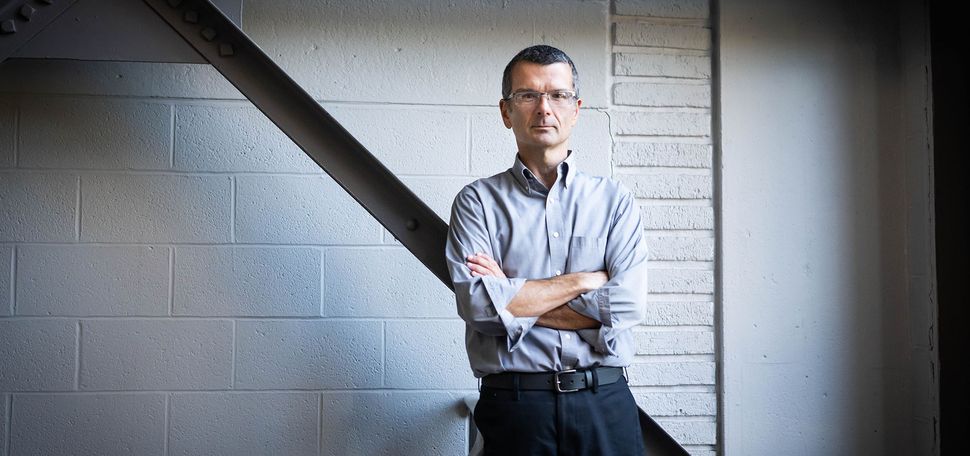 Photo: A man in a long-sleeve button down crossing his arms and leaning back. He has a very short haircut and glasses
