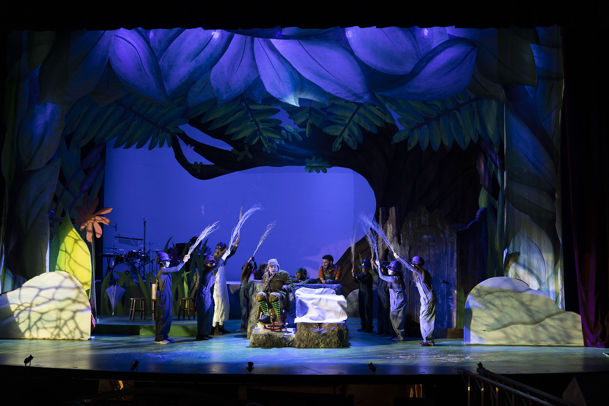 Photo: A wide shot of Wheelock Family Theatre's stage production of Frog and Toad. The stage is dark lit with huge trees in the background to create a cold, evening area.