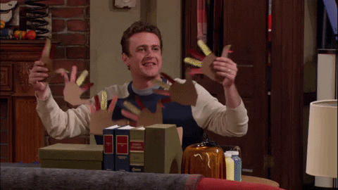 A GIF from how I met your mother of the main character unfolding a craft he made of colored paper turkeys all connected. He holds it up and smiles.
