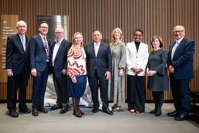 Photo: Nine people standing in front of a wall in the CDS Building at BU for a name unveiling ceremony