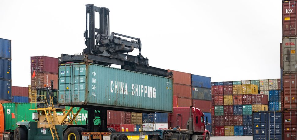 Photo: A cargo container labeled "China Shipping" being hoisted from a flatbad truck at a shipping port