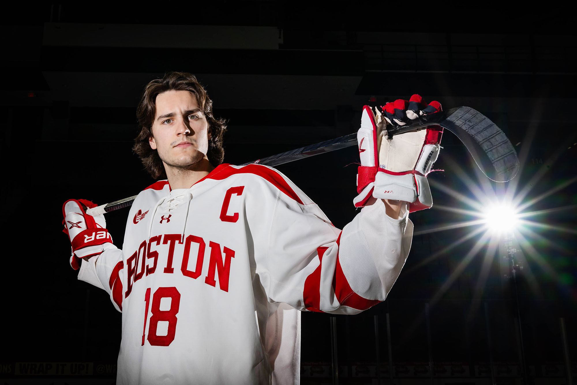 Photo: A hockey player posing in his Boston University uniform with a hockey stick in front of a black background