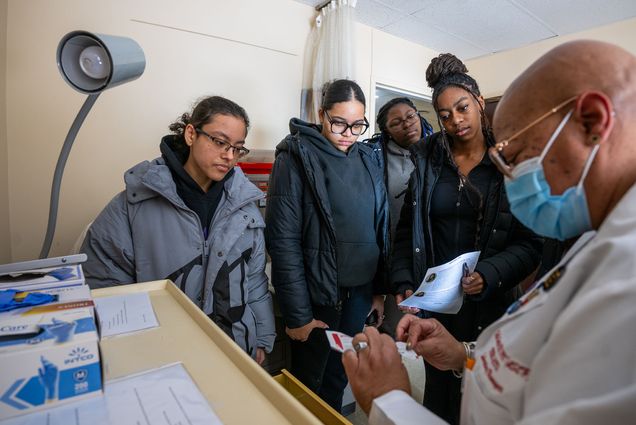 Photo: A man in a lab coat and mask showing a biopsy cart to a group of students