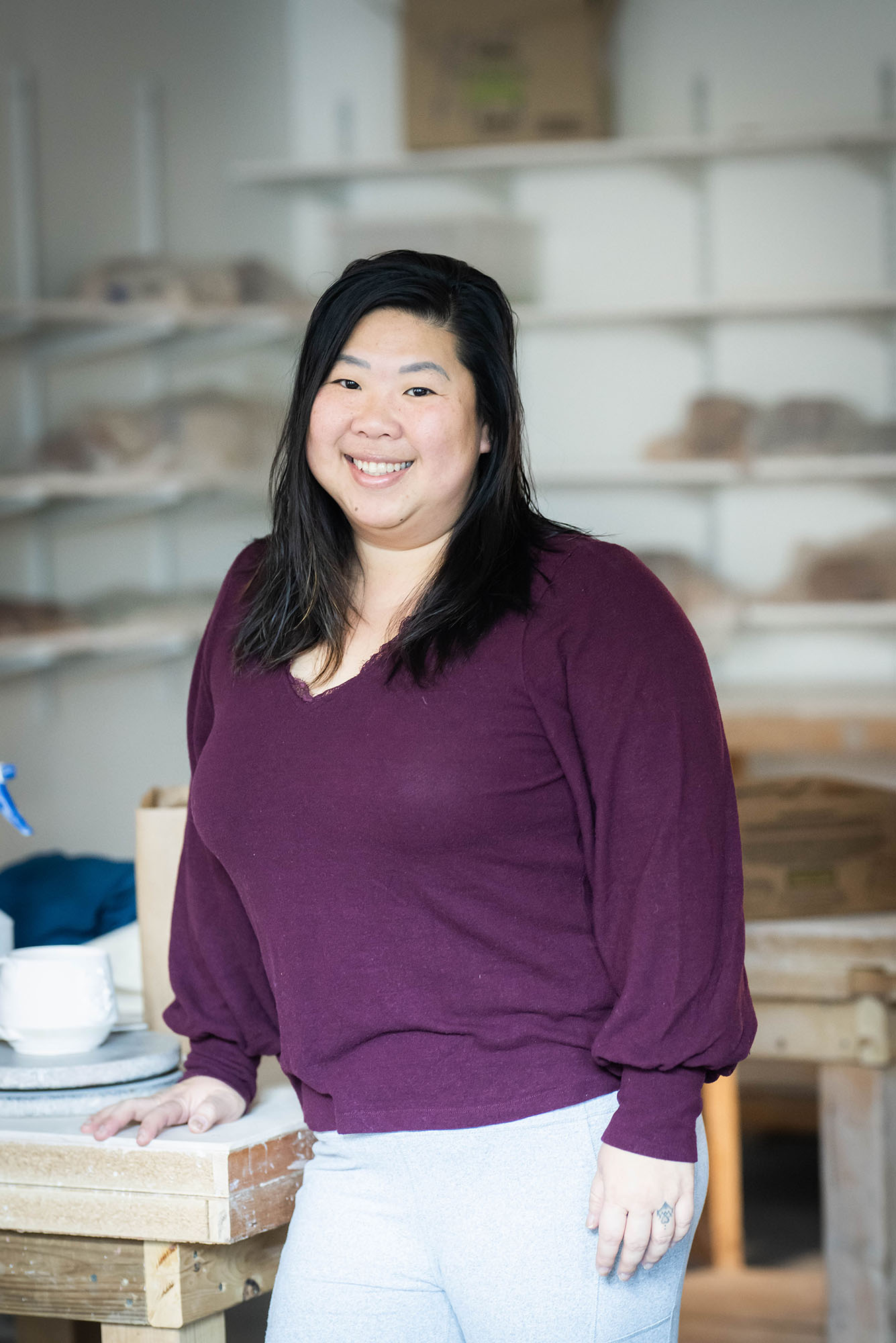 Photo: Kim Wong poses for a portrait photo in her pottery studio in a purple shirt.