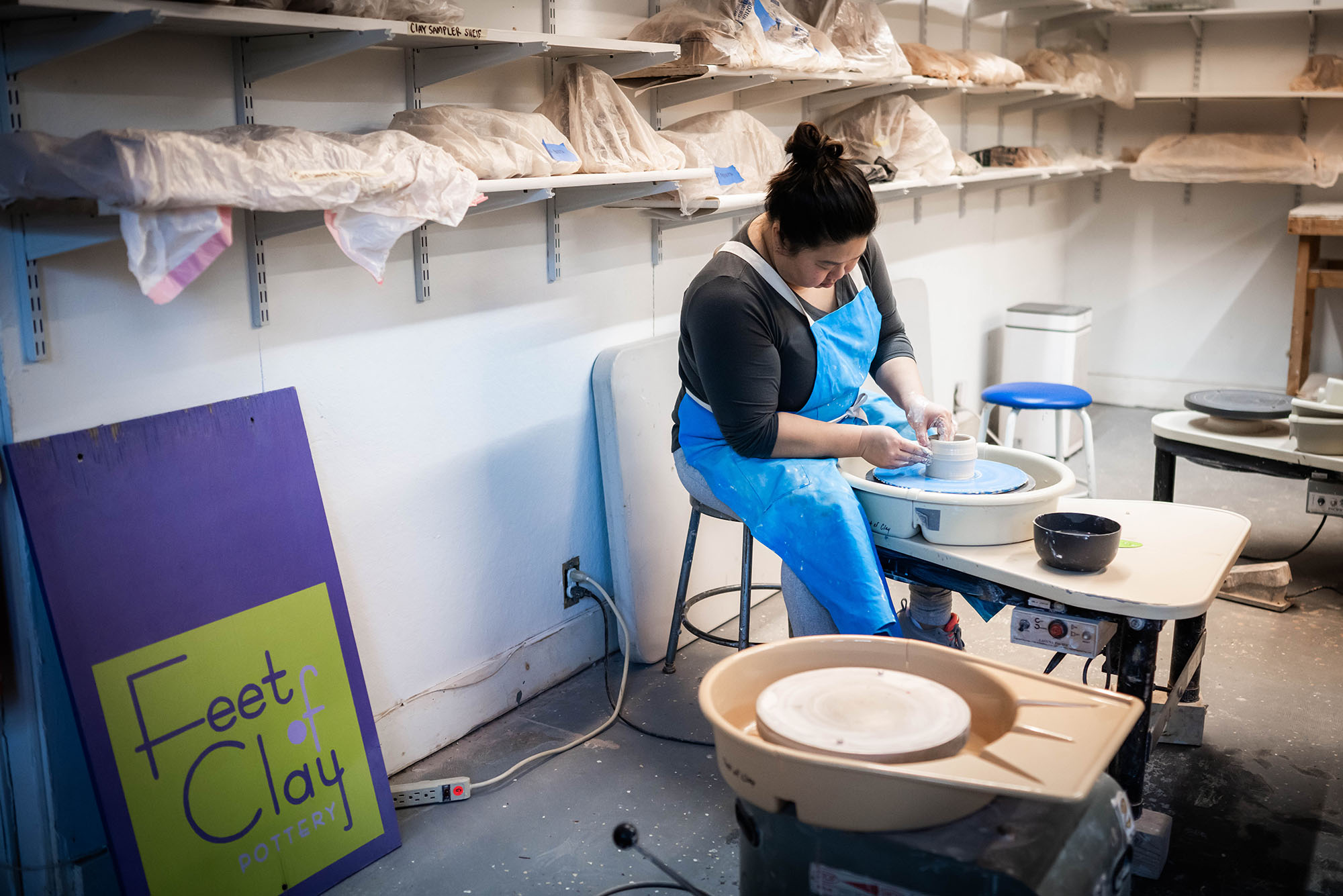 Photo: Kimberly Wong, a young woman wearing a black shirt, molding clay on a potter's wheel.