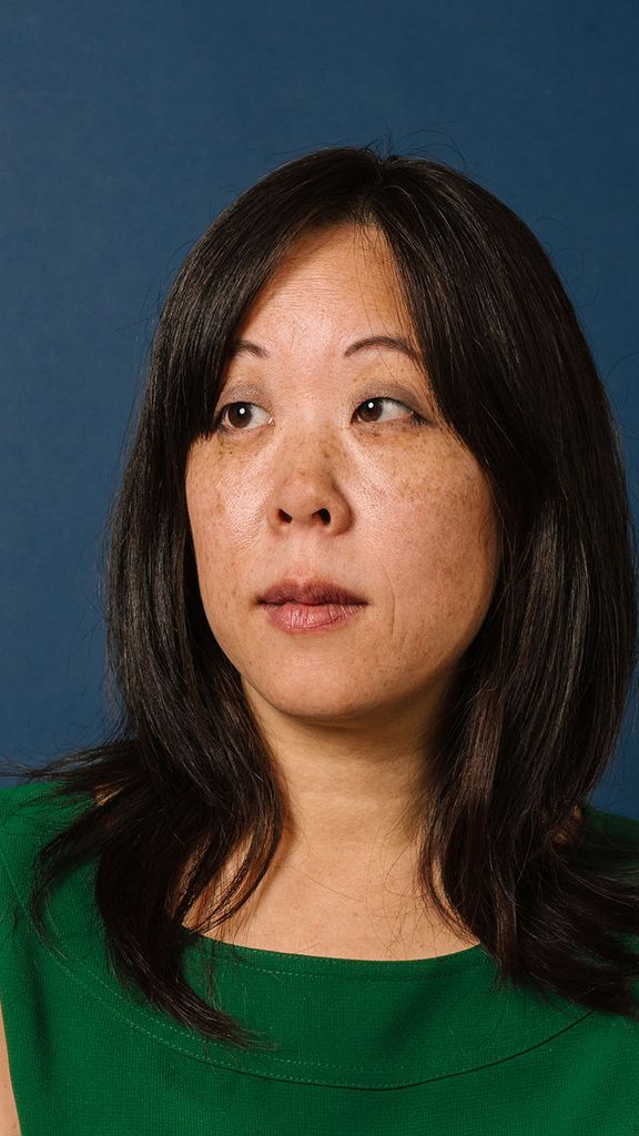 Photo: An Asian woman with mid-length dark hair in a green tank top posing in front of a dark background and looking off to the side