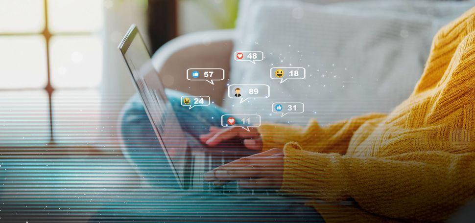 Photo: A person on their couch browsing social media on their laptop. Icons are coming out of hte computer showing likes and engagement with posts. There is a glitch overlay on the image
