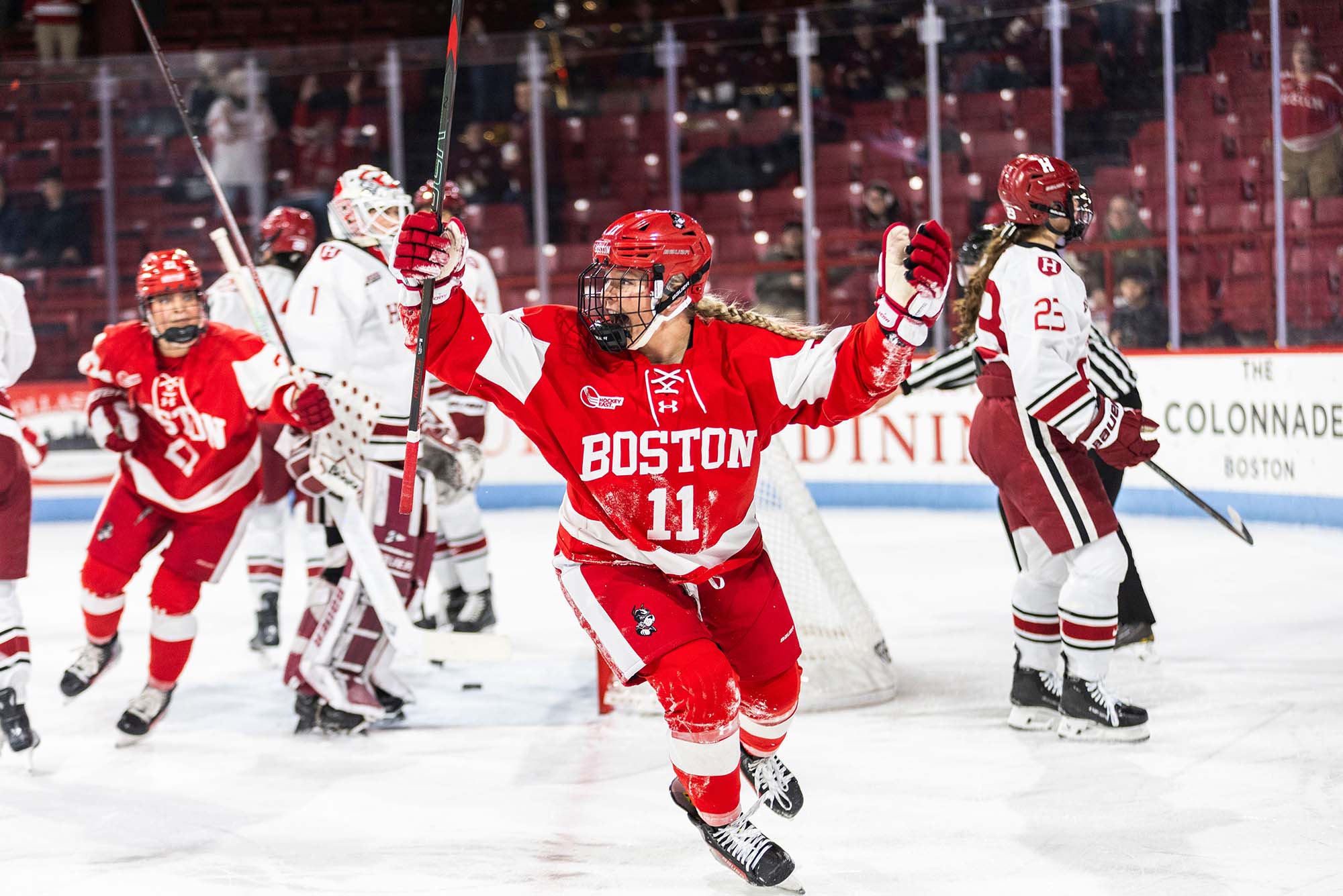 Photo: BU Women's Hockey player #11 celebrating on the ice with her arms raised in the air